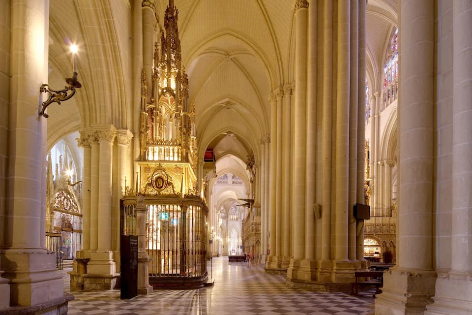 Interior de catedral com altos tetos abobadados, lustres elaborados e piso xadrez.