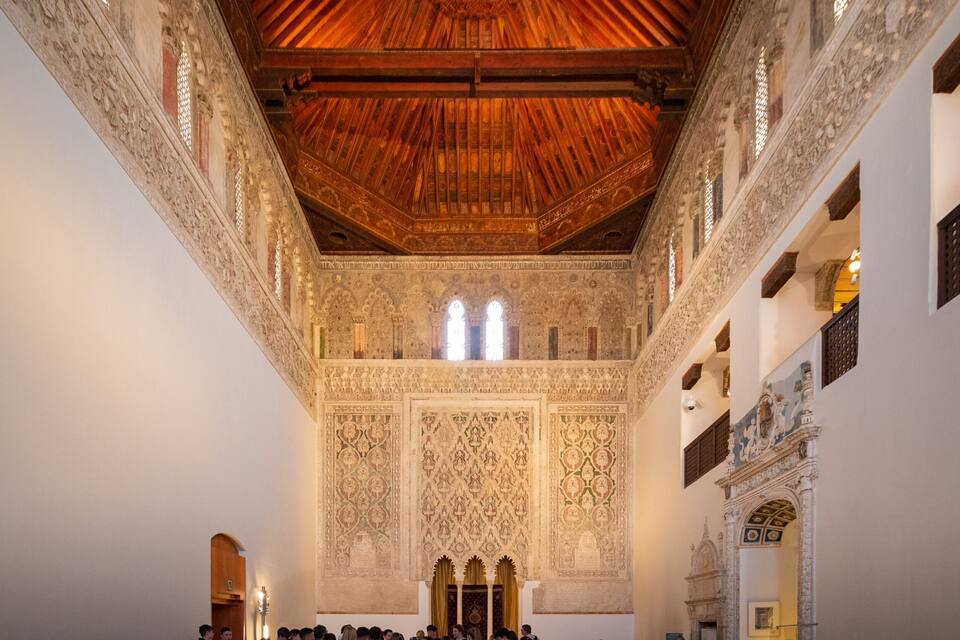 Un intérieur richement décoré, avec des motifs complexes sur le plafond et les murs, un plafond en bois et une allée centrale.