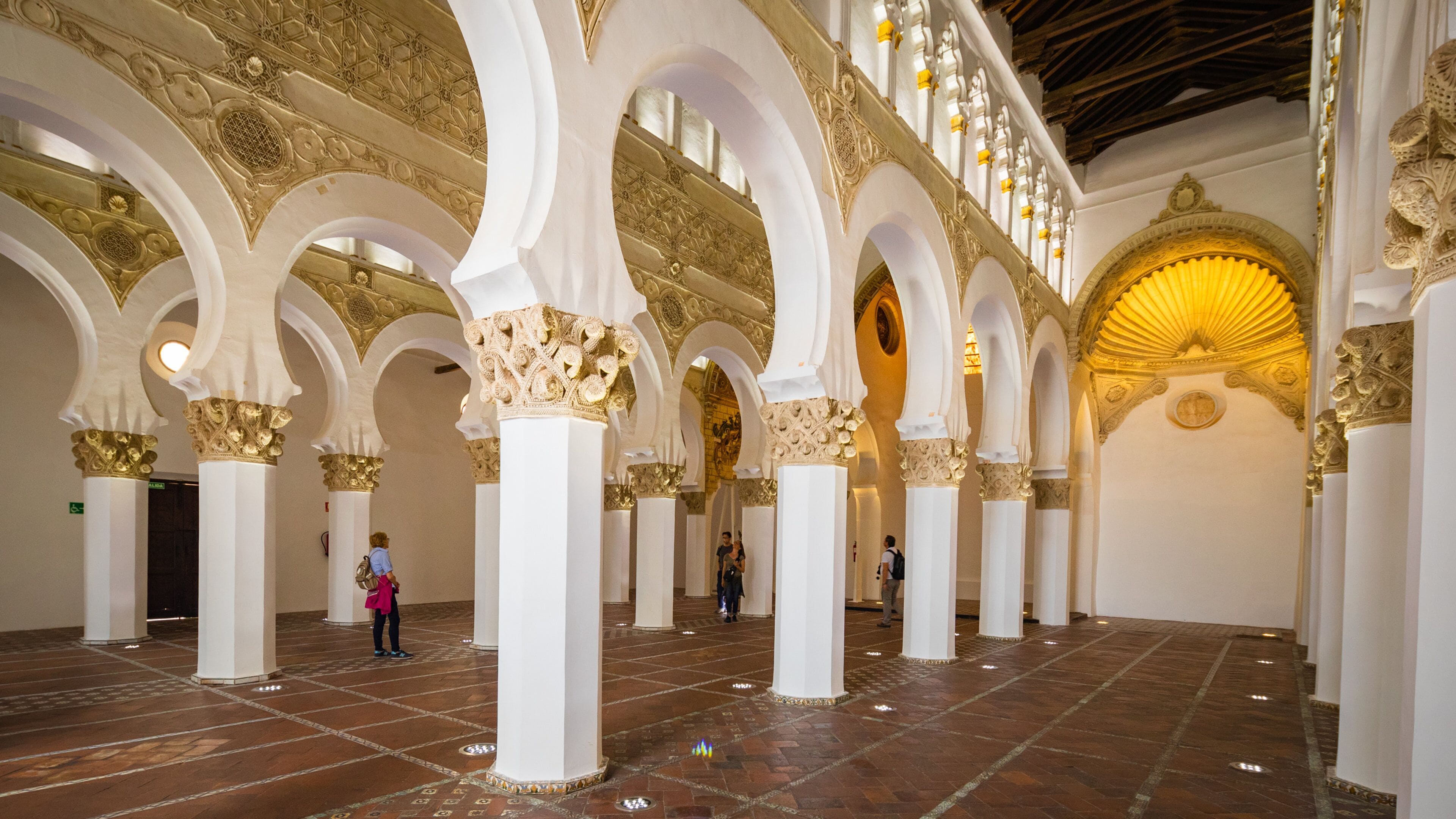 Een interieur met witte bogen en gouden details, een betegelde vloer en een grote gouden koepel.