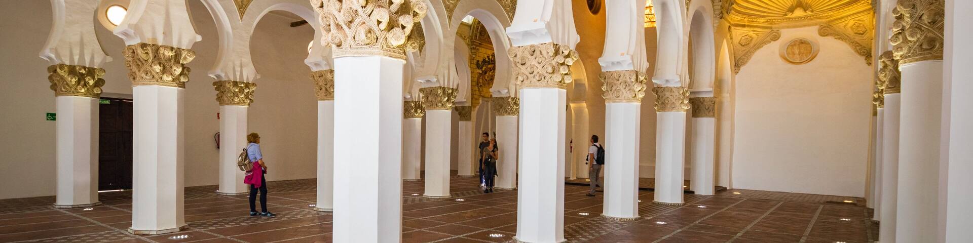 An interior with white arches and golden details, a tiled floor, and a large golden dome.
