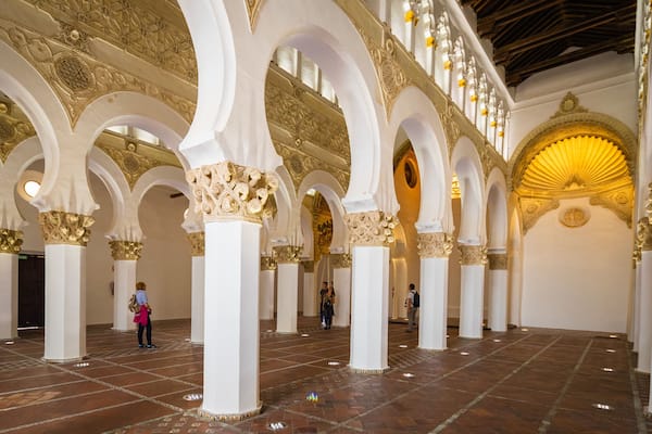 Interior com arcos brancos e detalhes dourados, piso ladrilhado e uma grande cúpula dourada.