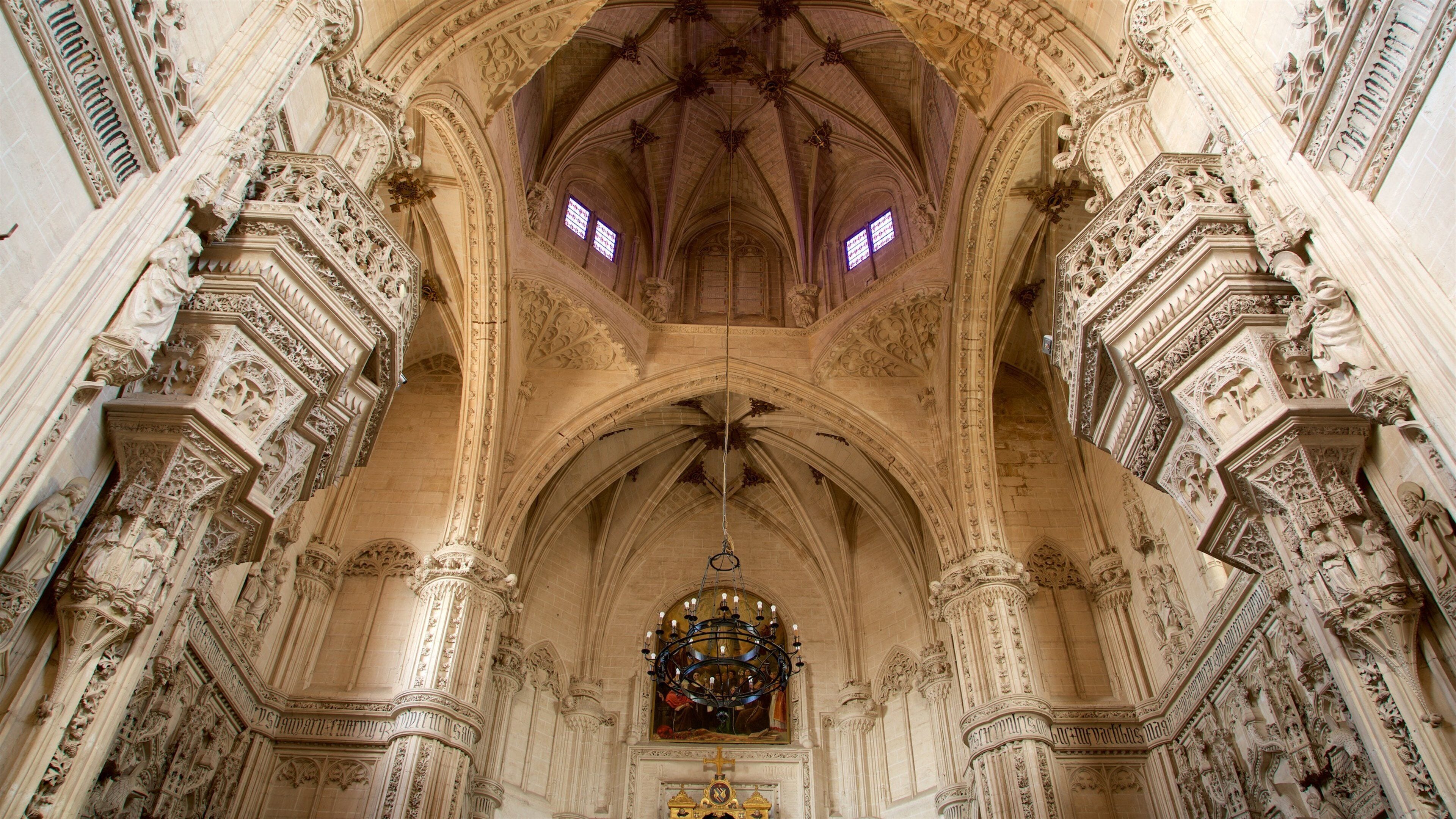 Een versierd kathedraalinterieur met ingewikkelde stenen beeldhouwwerken, een groot glas-in-loodraam en een hoog gewelfd plafond.
