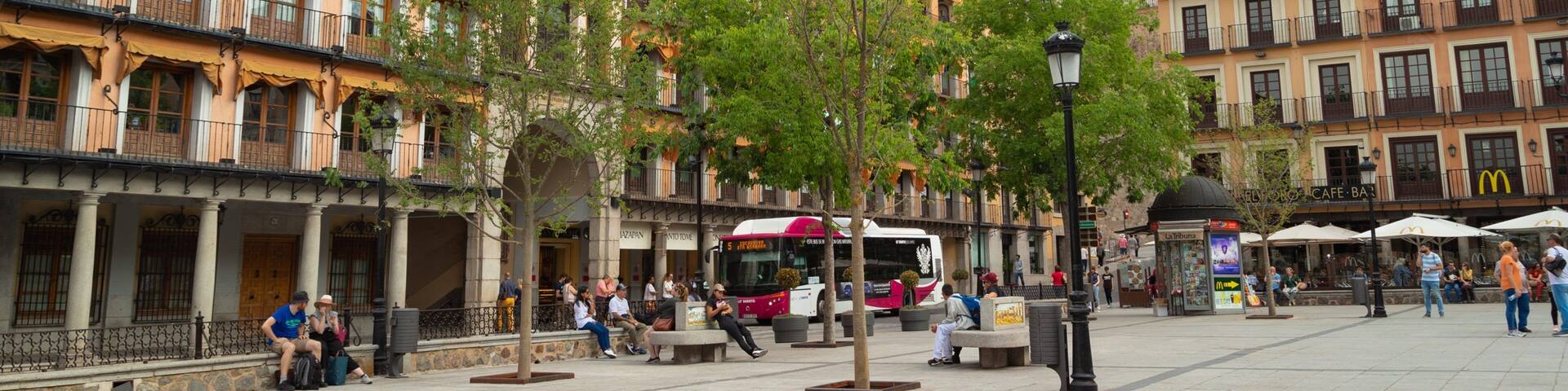 A plaza with historic buildings, a clock tower, and a bus.