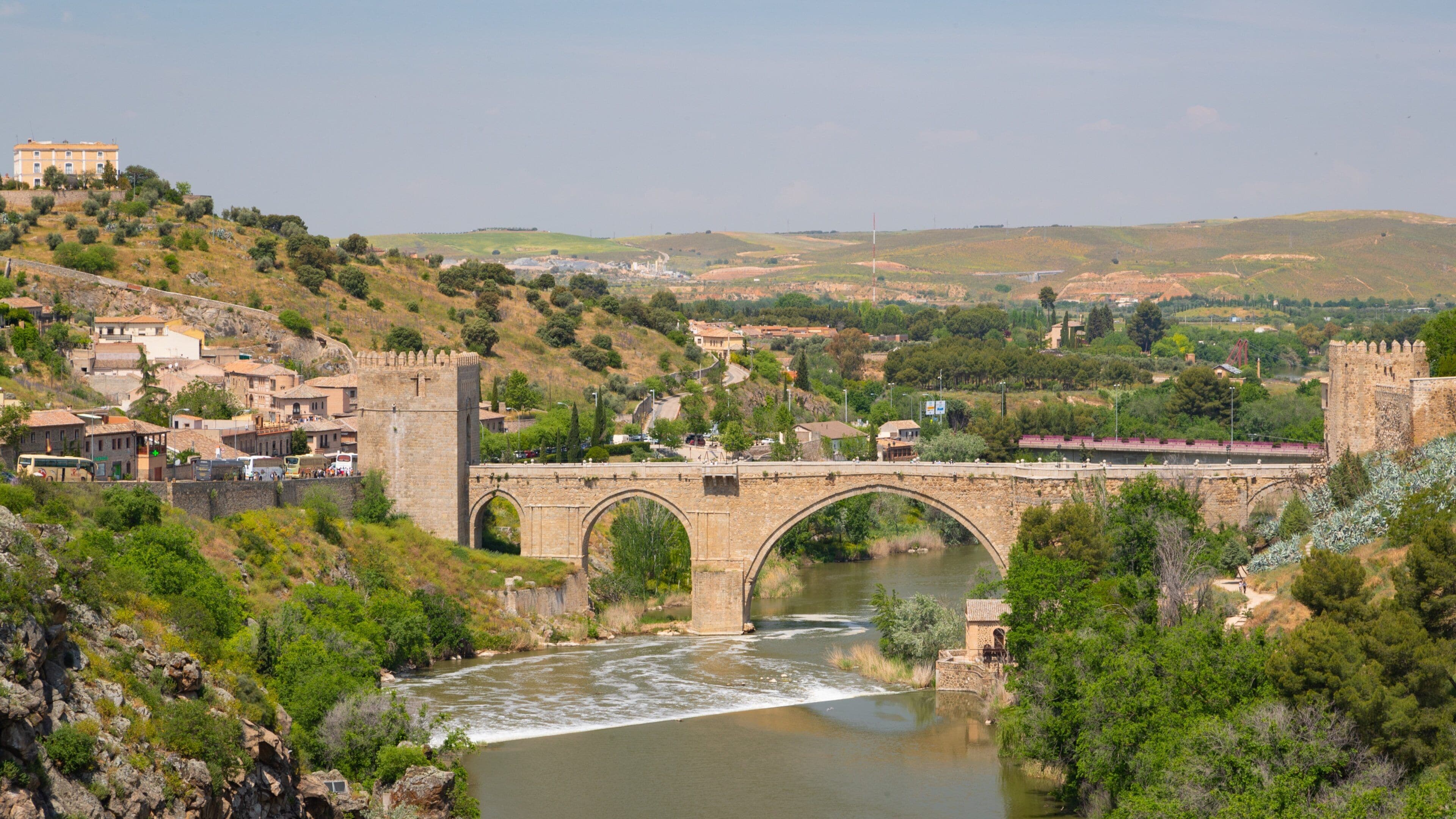 A stone bridge over a river with a town and castle in the background.