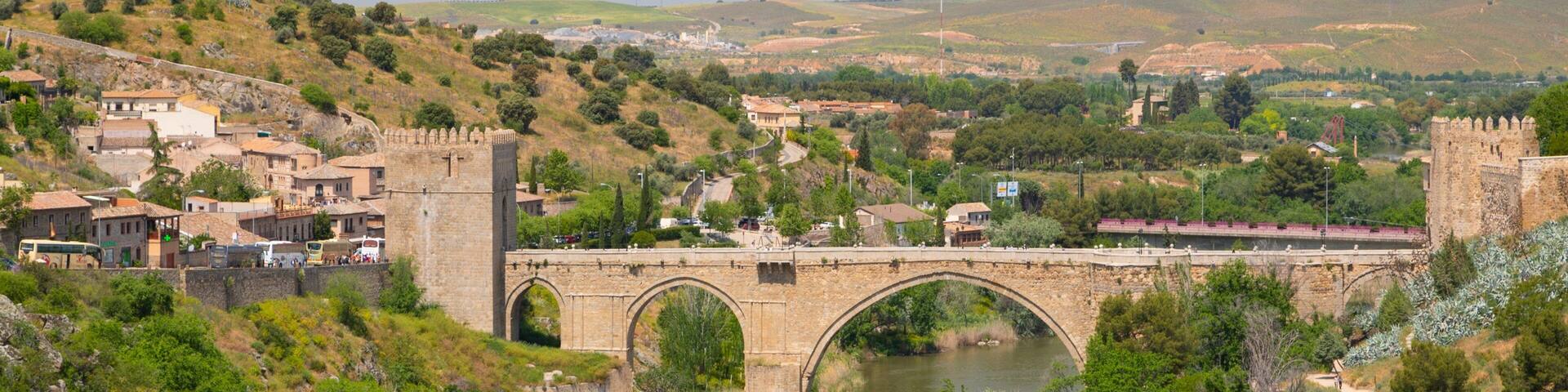 A stone bridge over a river with a town and castle in the background.