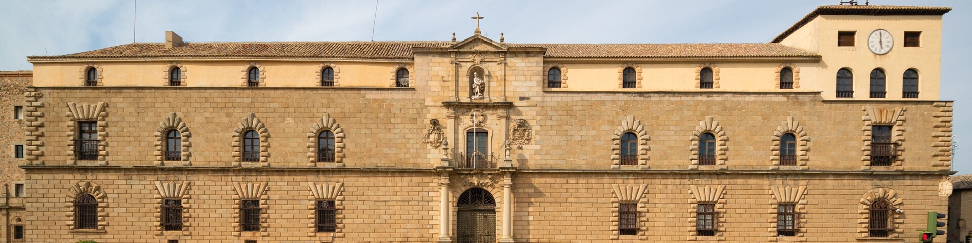 Um grande edifício histórico com uma torre de relógio, janelas em arco e uma entrada central.