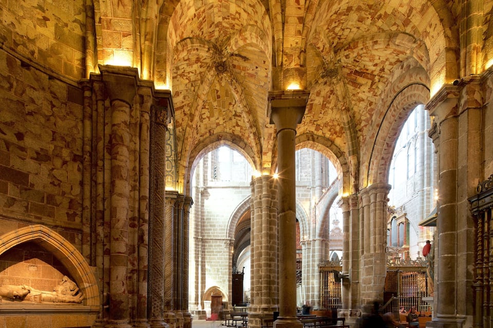 Interior de una catedral con altos techos abovedados, grandes columnas de piedra y ventanas en arco.
