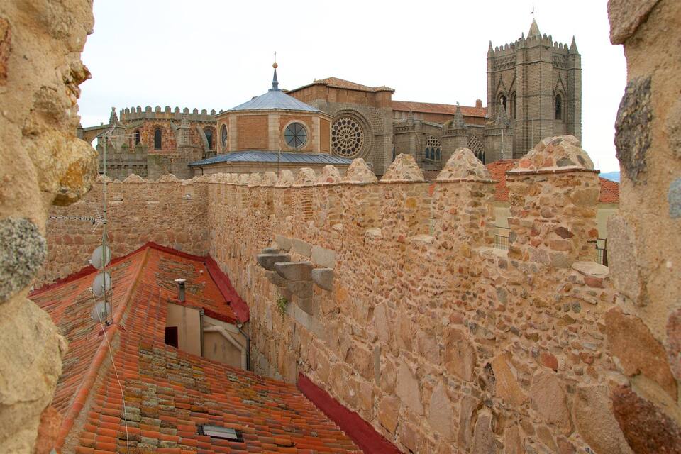 Un muro de piedra histórico con tejados rojos que conduce a una gran iglesia con un ventanal circular destacado y una aguja.