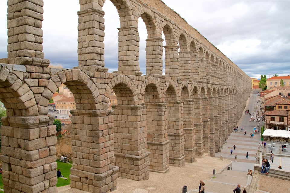 Un antico acquedotto con diverse arcate, una piazza lastricata con persone e edifici circostanti.