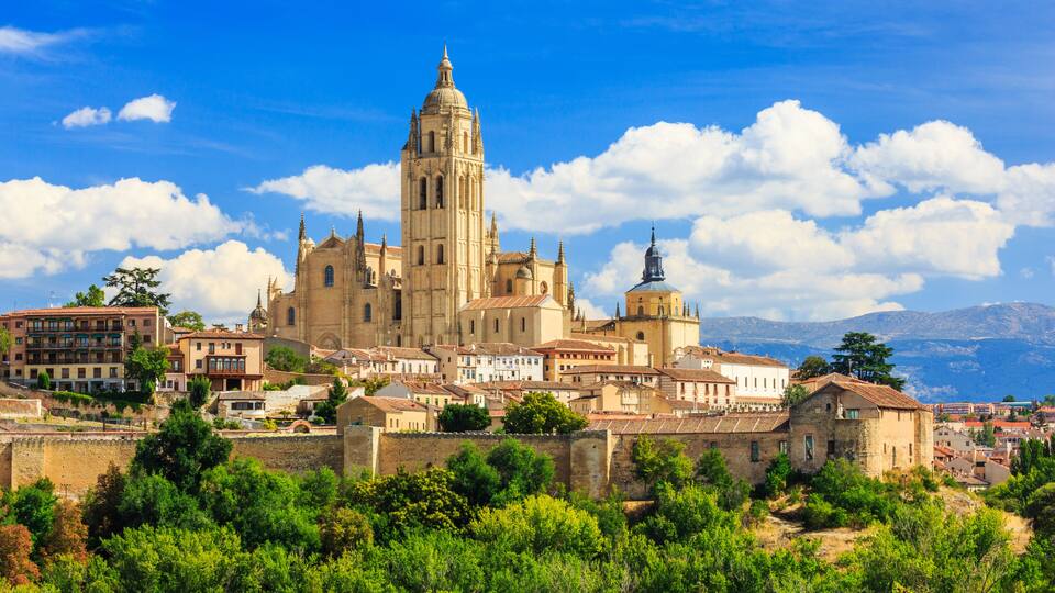 A historic cathedral with a prominent bell tower, surrounded by lush greenery and traditional buildings.