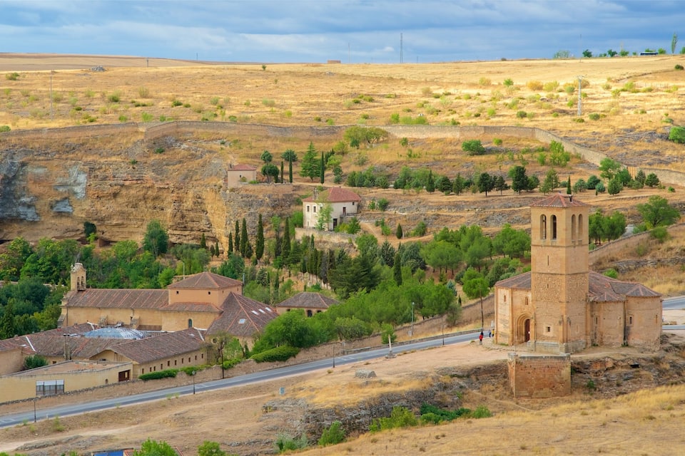 A village with a prominent church tower, surrounded by dry hills and sparse vegetation.