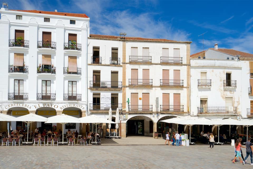 Une place avec des tables à l’extérieur et un bâtiment blanc doté de balcons.