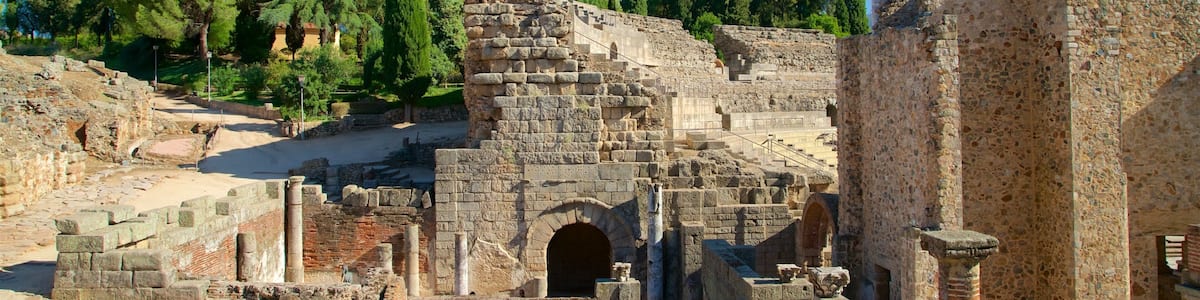 Des ruines antiques, avec des colonnes et des arches, entourées d’arbres et surplombées par un ciel dégagé.