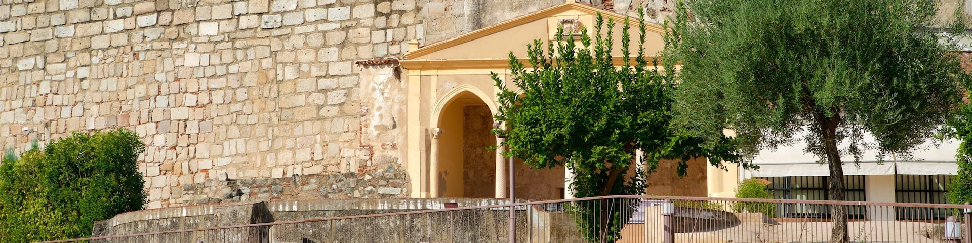 A historic stone wall with an arched entrance and a tree in the foreground.