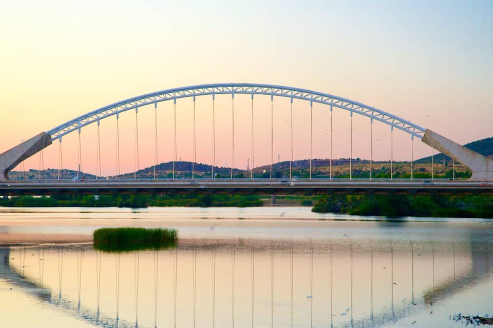 A large, arched bridge over a river with hills in the background.
