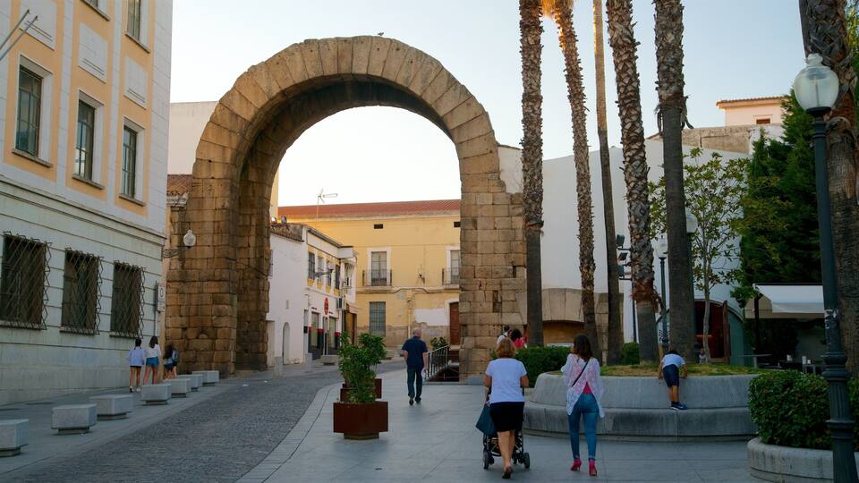 Un arco en una zona peatonal con gente caminando, palmeras y edificios al fondo.