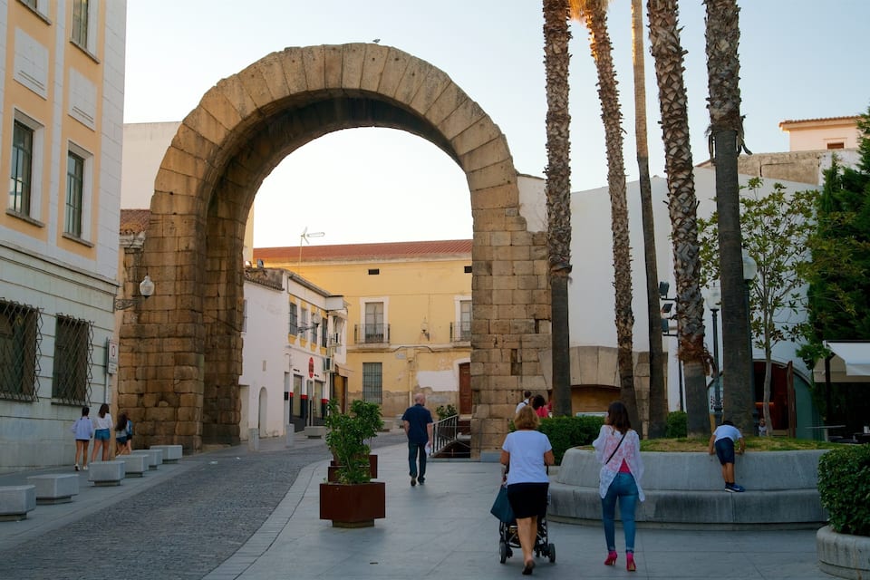 An archway in a pedestrian area with people walking around, palm trees, and buildings in the background.