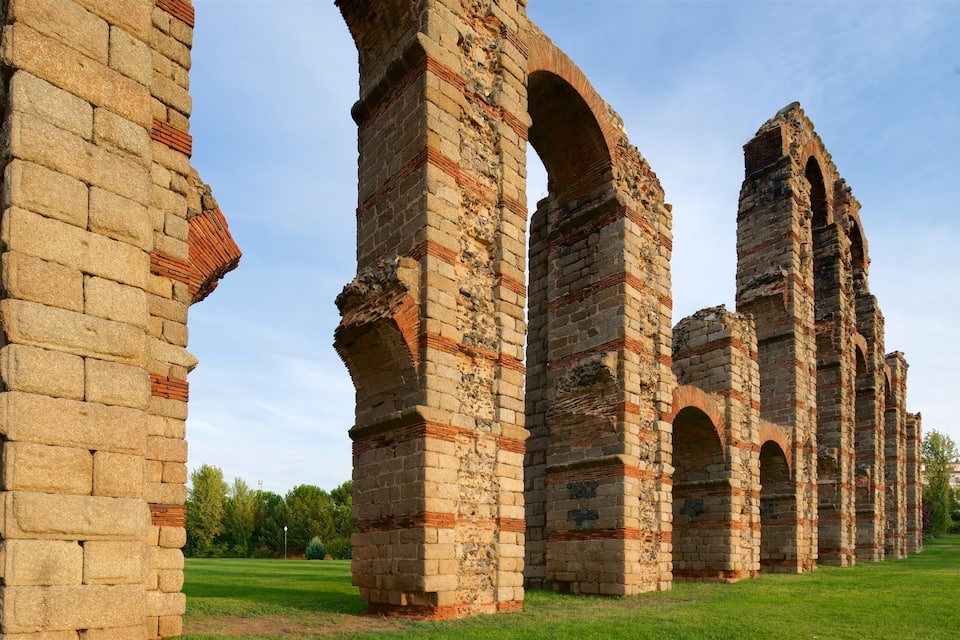Ancient stone ruins with arches and brickwork, surrounded by a grassy field and trees.