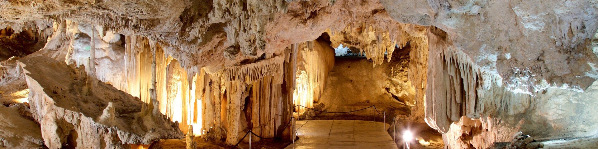 A cave with stalactites and stalagmites, illuminated by artificial lighting.
