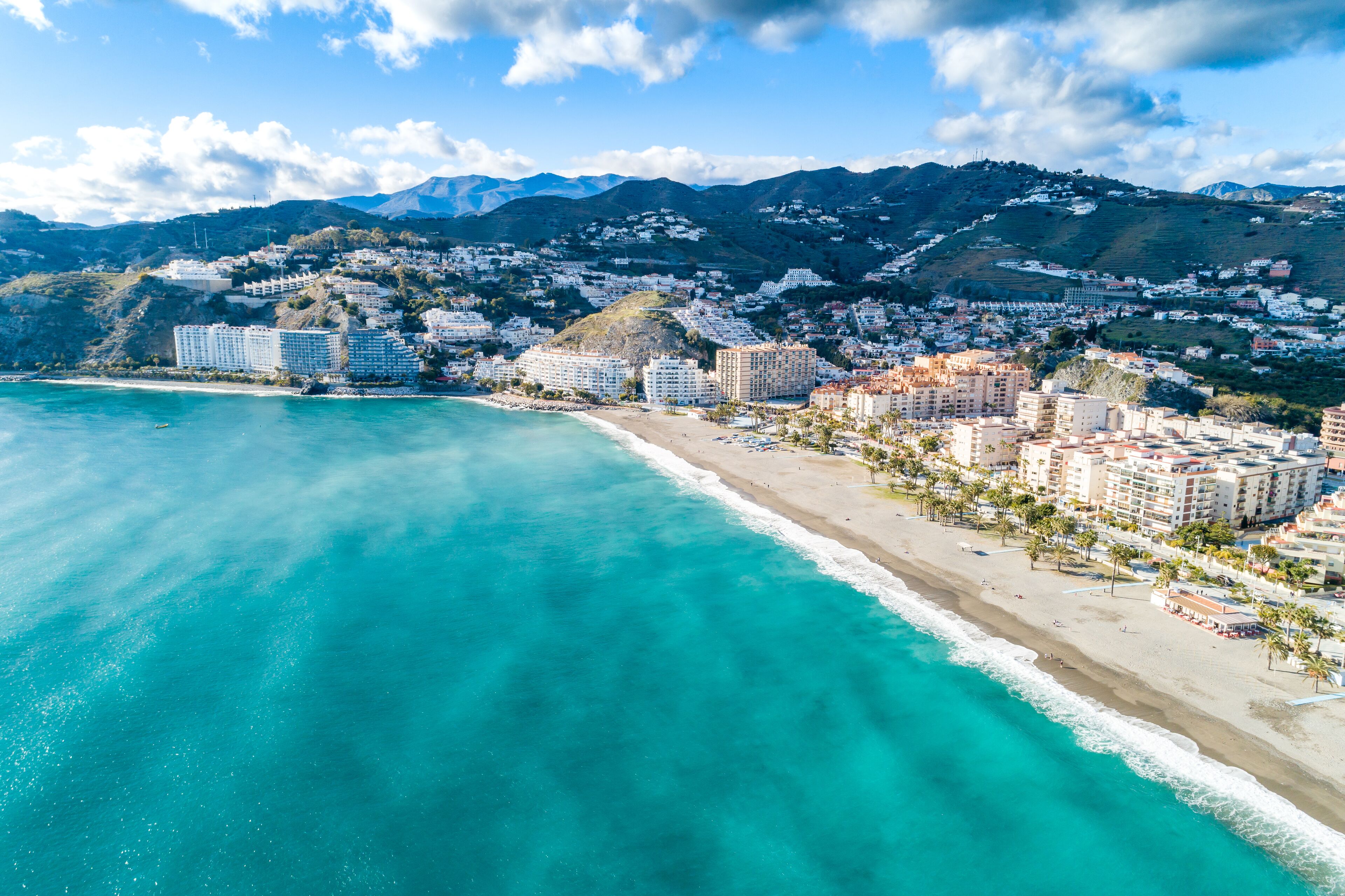 A coastal city with a beach, buildings, and mountains in the background.