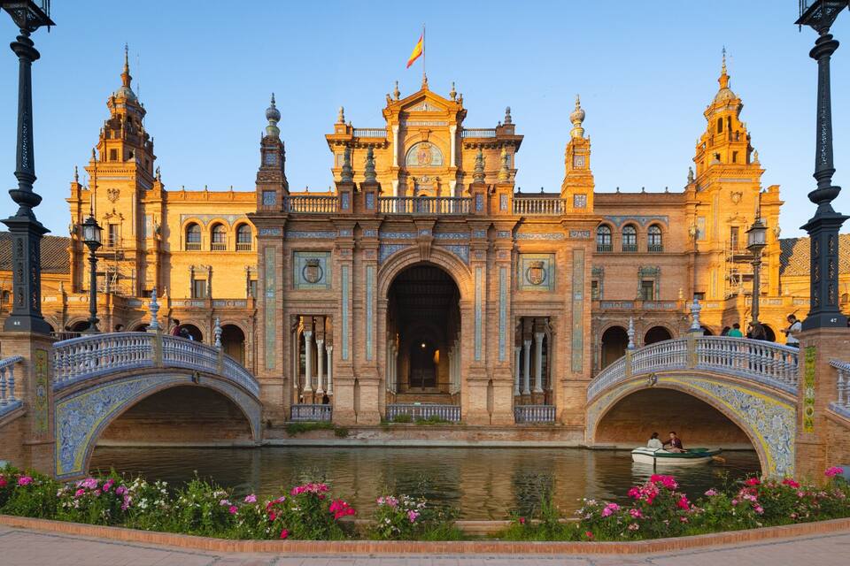 A historic building with ornate architecture, a central archway, and two bridges over a canal.