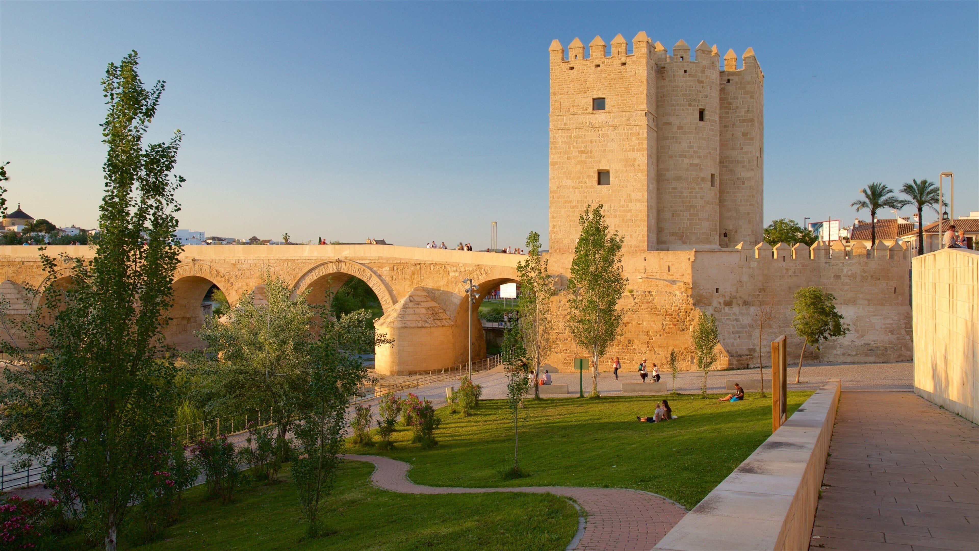 A historic stone bridge with arches, a tall tower, and a well-maintained grassy area with pathways.