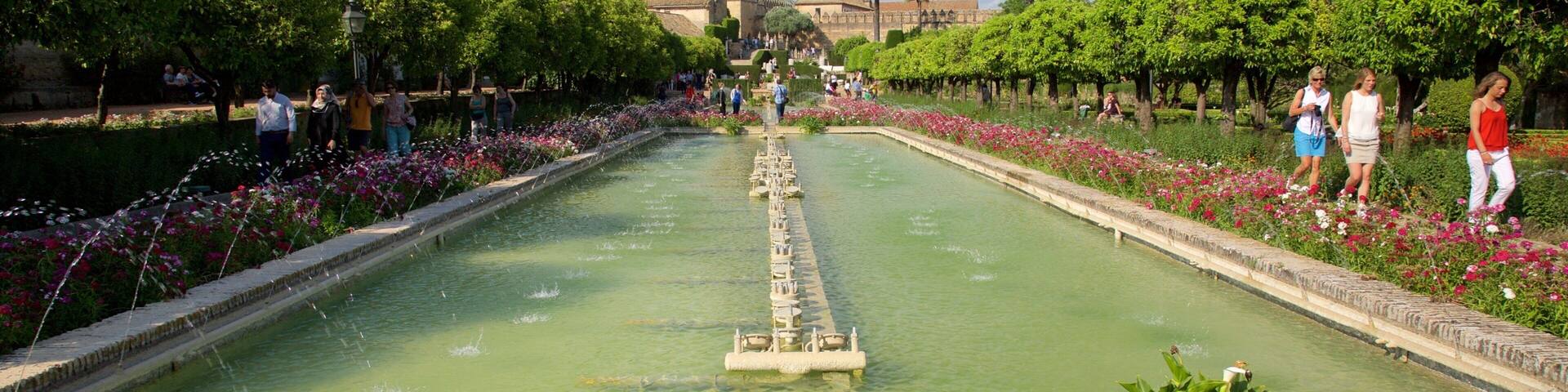 A large rectangular water feature with a central fountain, surrounded by well-manicured flower beds and trees.