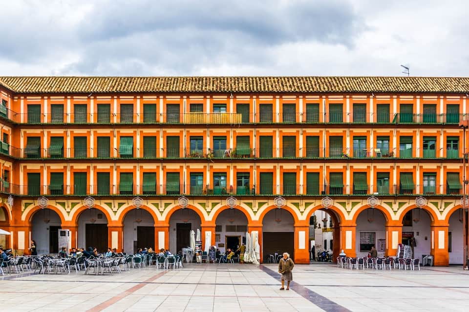 A courtyard with a building featuring orange and green arches and a tiled roof.