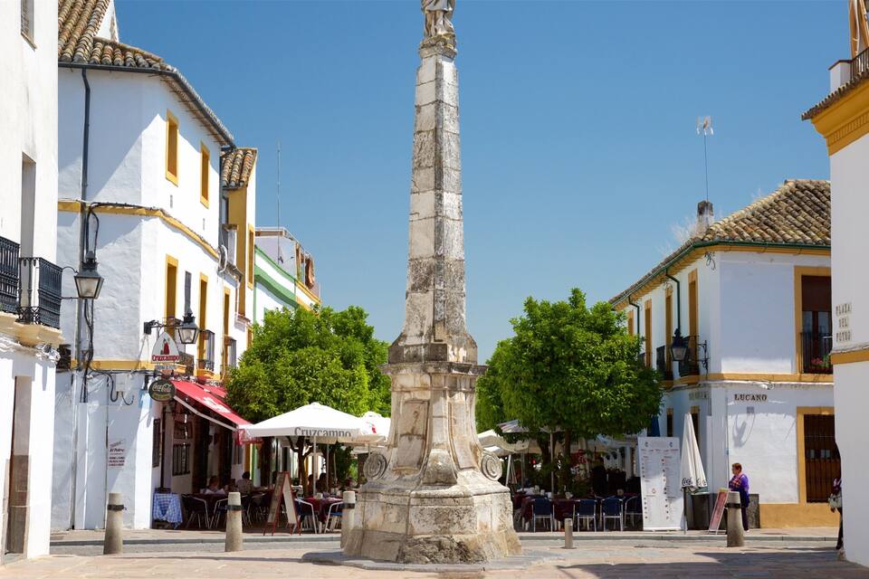 A historic square with a central monument, white buildings with yellow trim, outdoor cafes, and a clear blue sky.