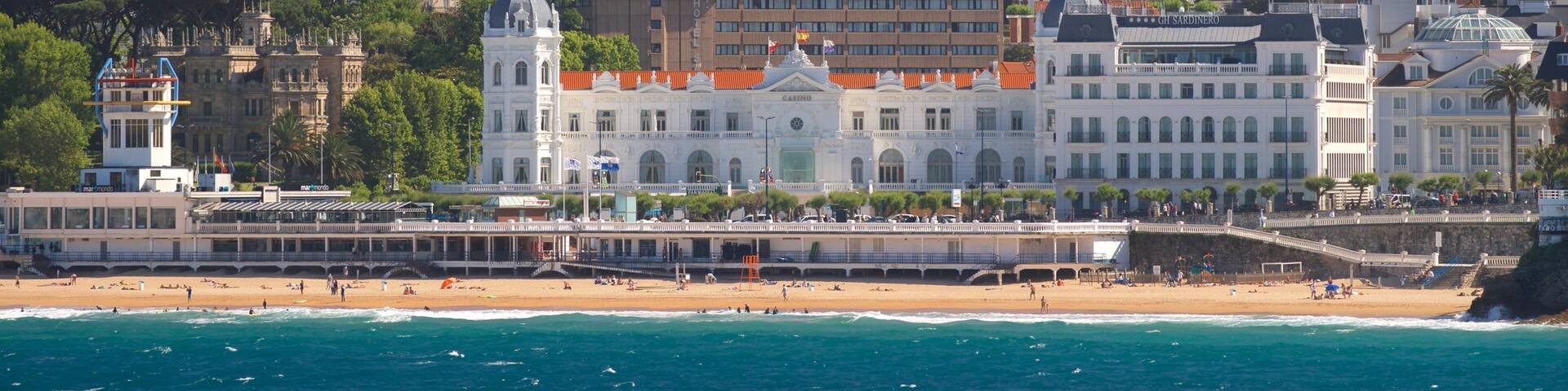 A coastal cityscape with a prominent white building with a dome, a beach, and a sea view.
