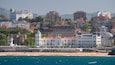 A coastal cityscape with a prominent white building with a dome, a beach, and a sea view.