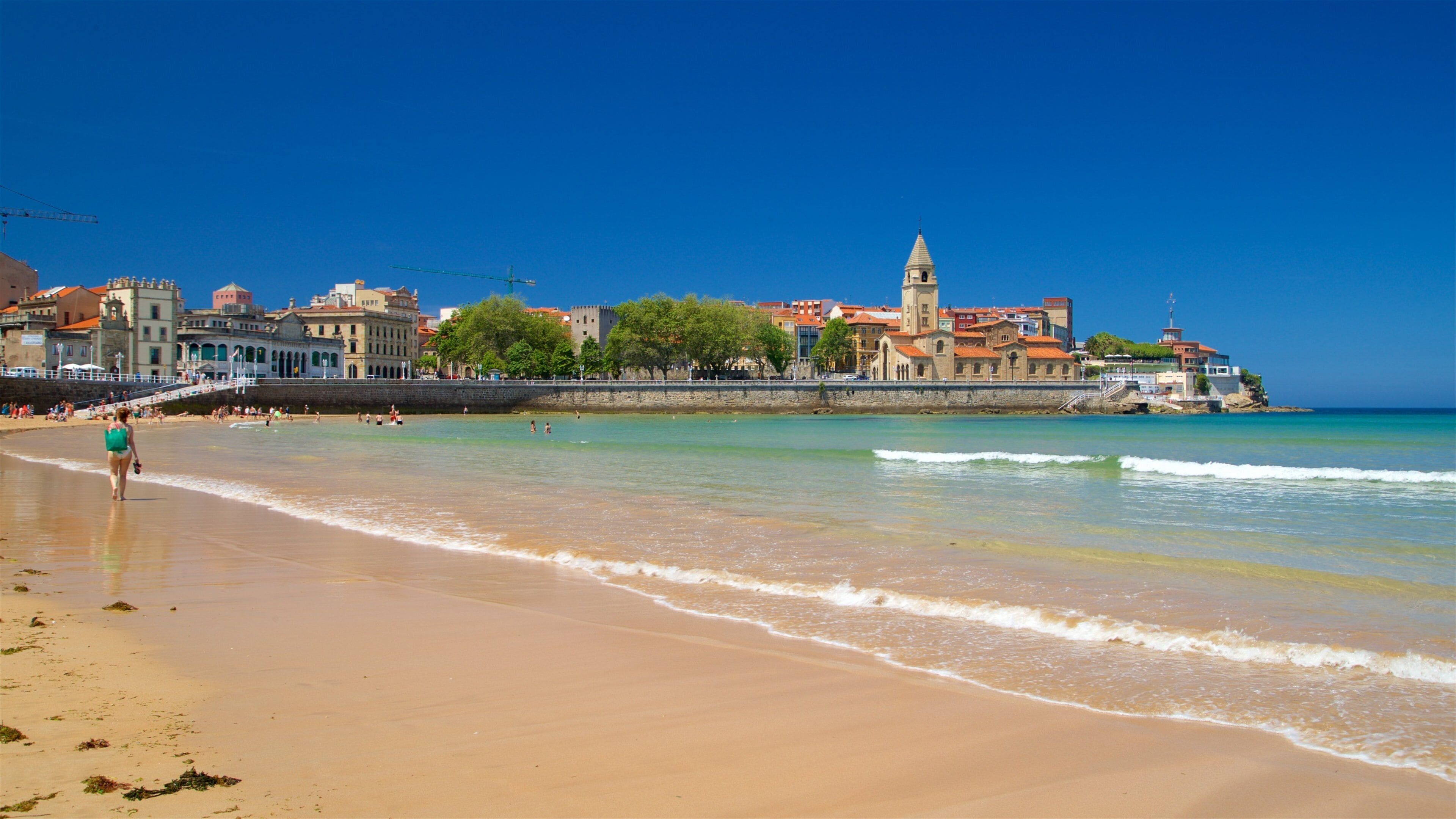 A beach with a cityscape in the background, including a prominent tower and various buildings.