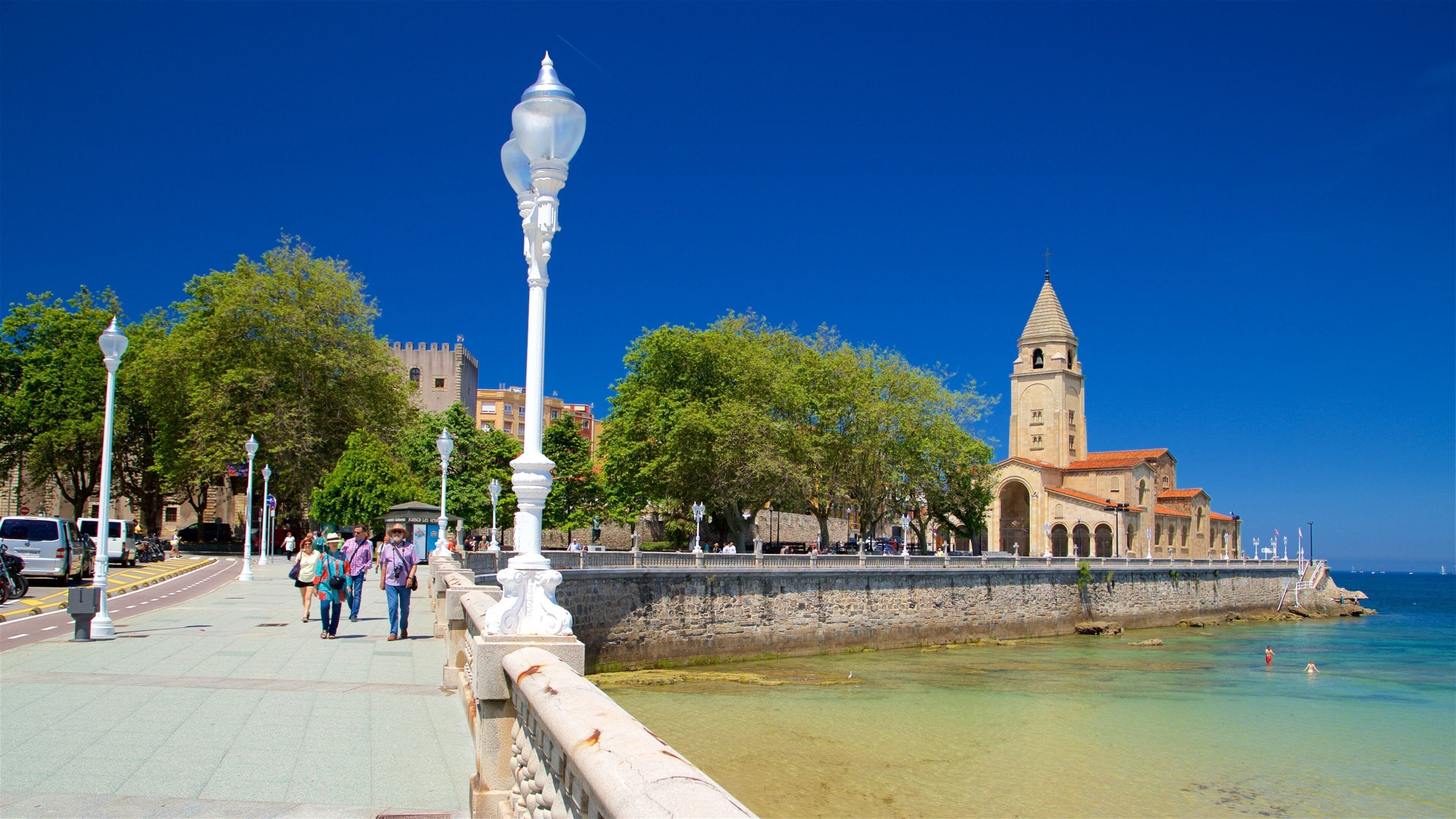 Um calçadão costeiro com uma torre histórica, céu azul límpido e mar calmo.