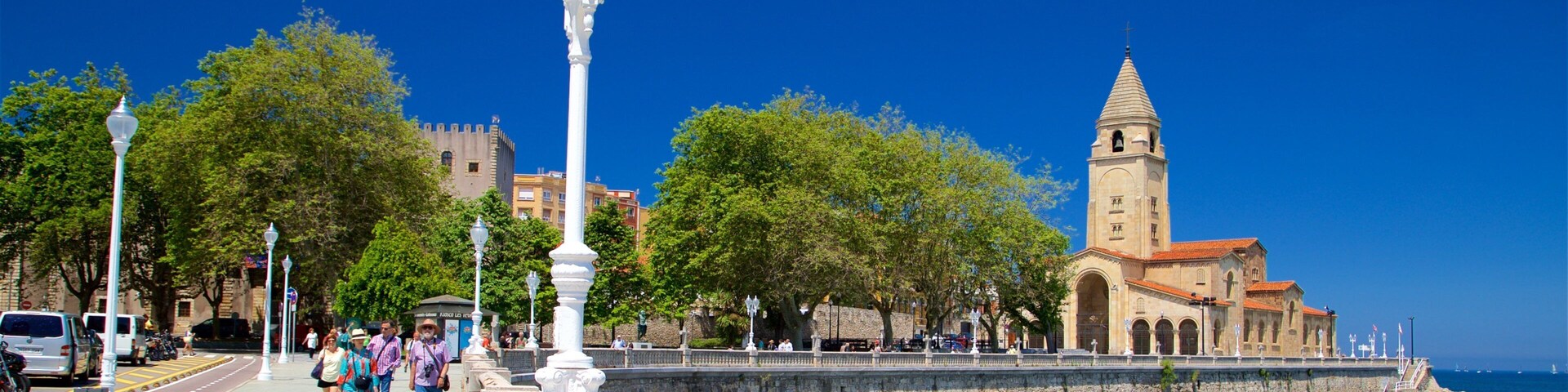 Um calçadão costeiro com uma torre histórica, céu azul límpido e mar calmo.