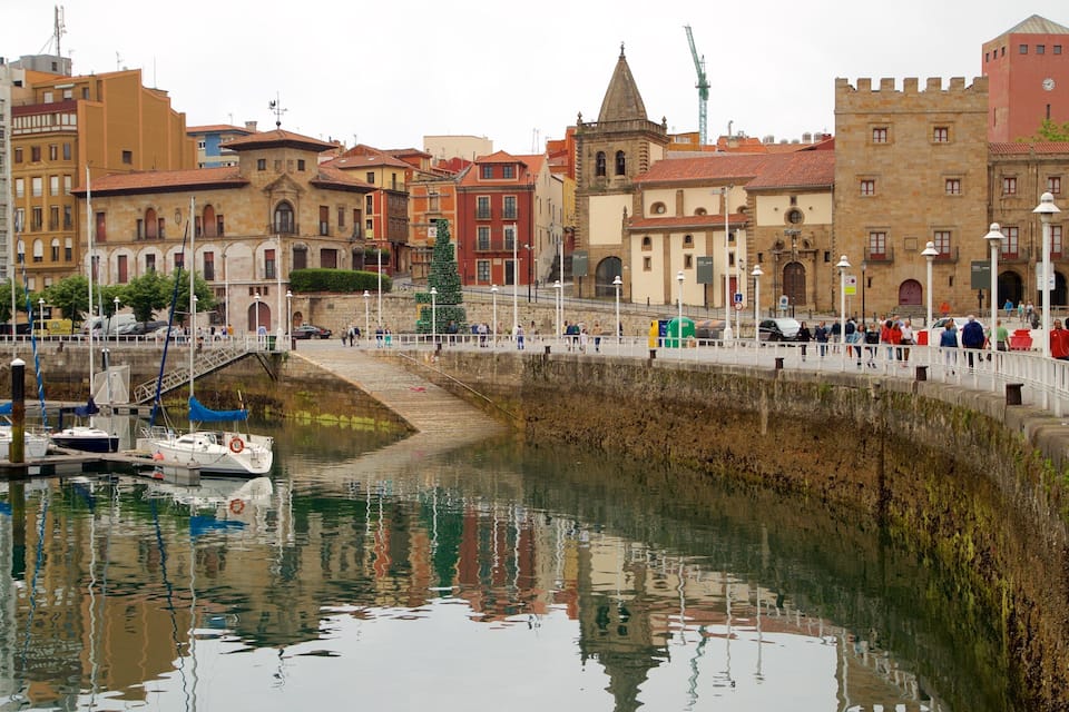 A waterfront with historic buildings, a bridge, and boats docked at the marina.