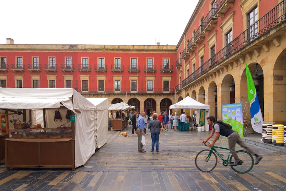 A bustling outdoor market with stalls, a cyclist, and historic buildings in the background.