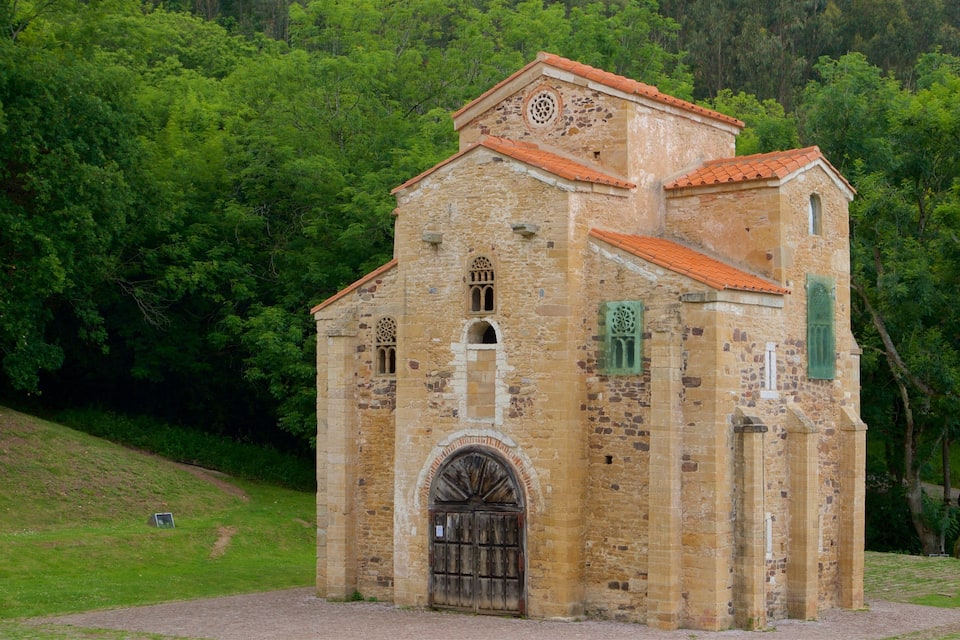 En historisk kyrka byggd av sten, med ett rött tegeltak, omgiven av frodig grönska.