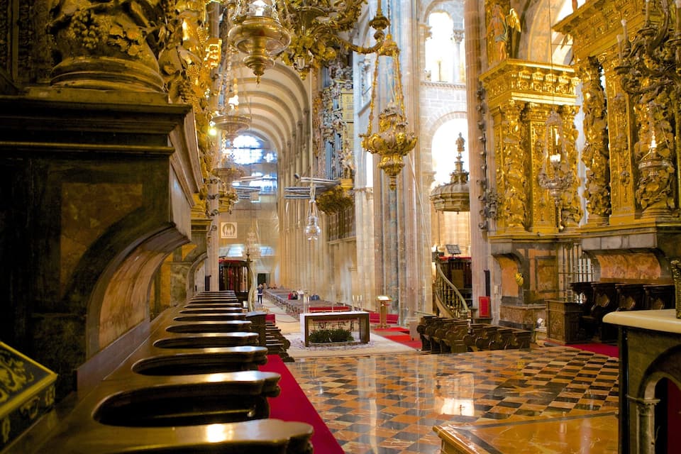 An ornate church interior with a checkered floor, rows of pews, and elaborate golden decorations.