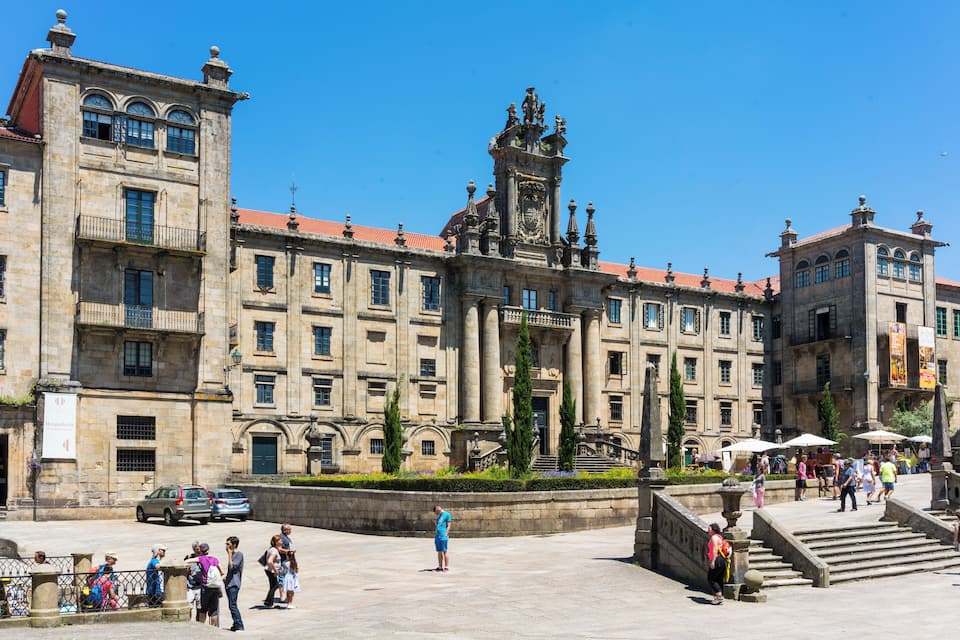 A historic building with a clock tower, surrounded by a plaza with people and cars.