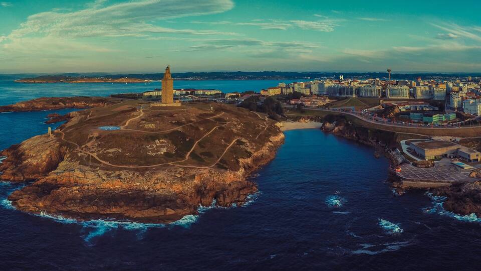 An aerial view of a coastal city with a prominent lighthouse, rocky coastline, and a mix of urban and natural landscapes.