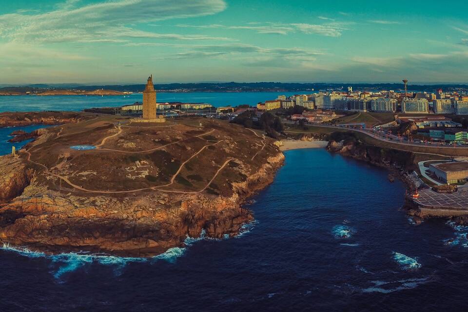 An aerial view of a coastal city with a prominent lighthouse, rocky coastline, and a mix of urban and natural landscapes.