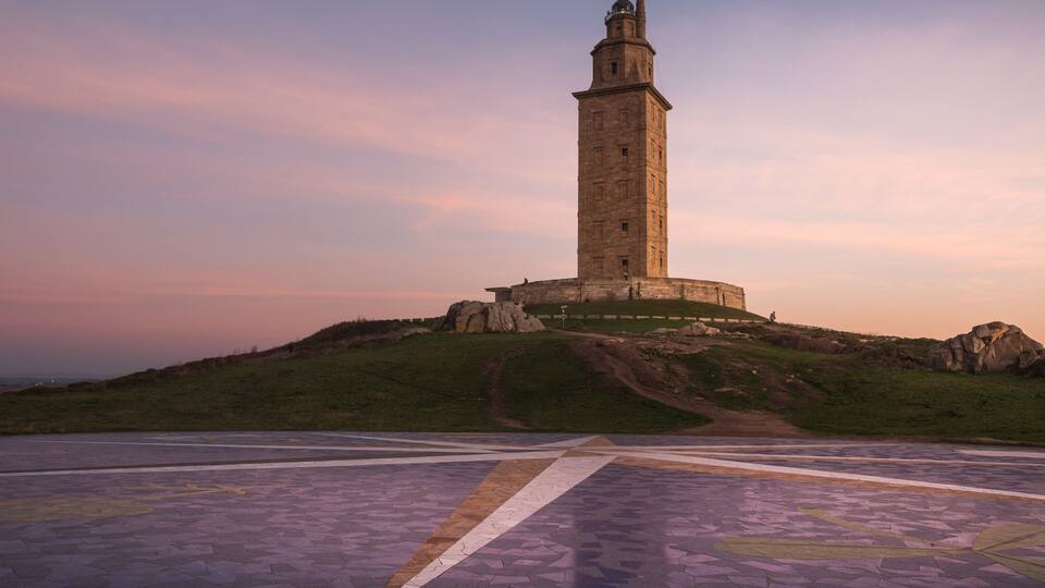 A tall stone tower on a hill with a paved area in the foreground.