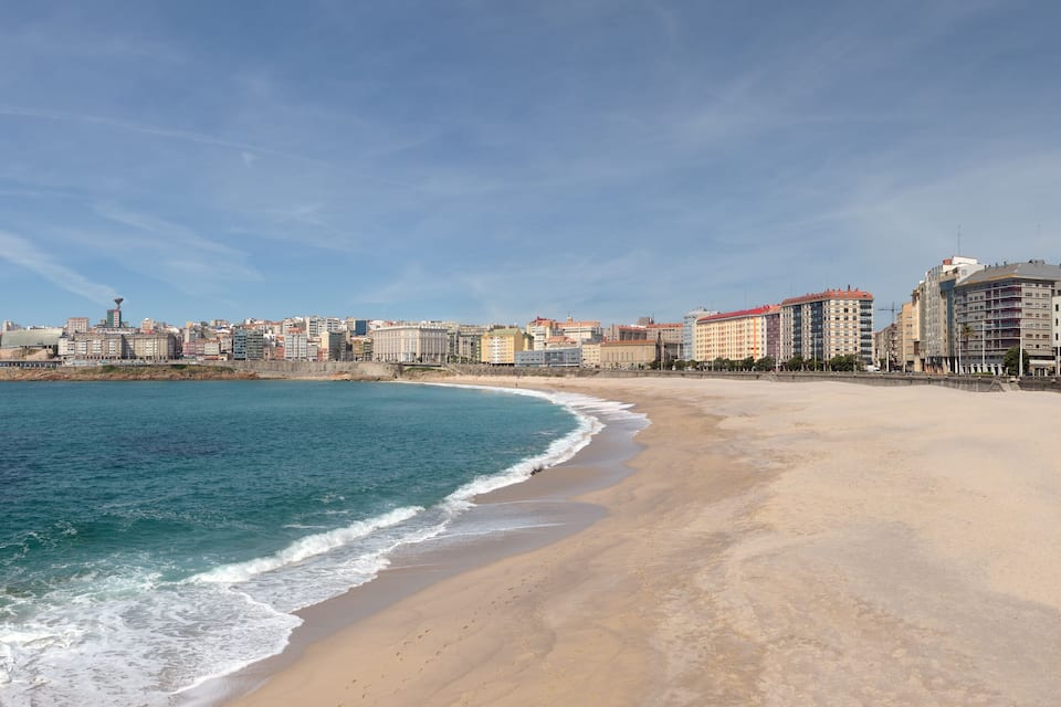A coastal cityscape with a sandy beach, ocean waves, and a variety of buildings.