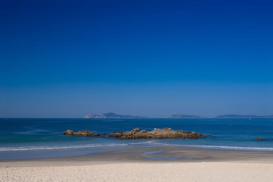 A beach with clear blue water, sandy shore, and rocky outcrops.