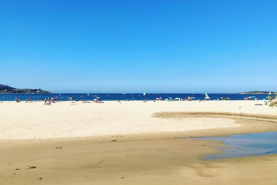 A beach with clear skies, calm waters, and a few sailboats.