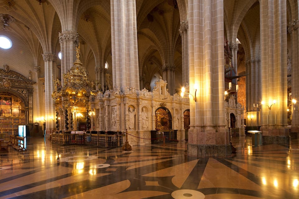 Een statig kathedraalinterieur met hoge gewelfde plafonds, versierde zuilen en een rijk gedecoreerd altaar.