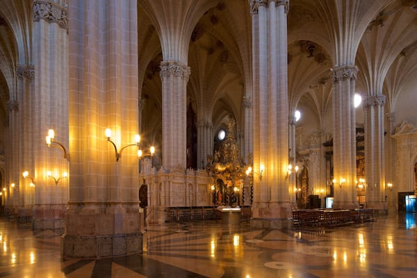 Un vaste intérieur de cathédrale, avec de hauts plafonds en voûte, des colonnes richement décorées et un autel central.