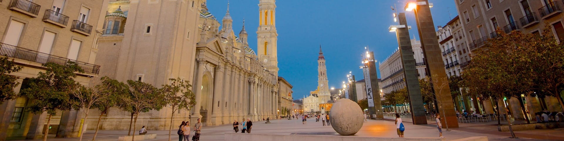 A historic plaza with ornate buildings, a large spherical sculpture, and a clear blue sky.
