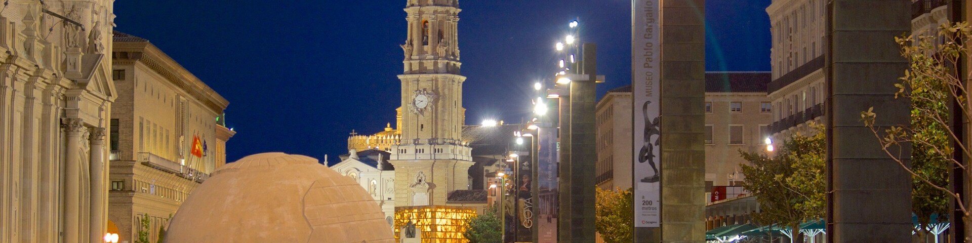 A large spherical sculpture in a public square with historic buildings and a clock tower in the background.
