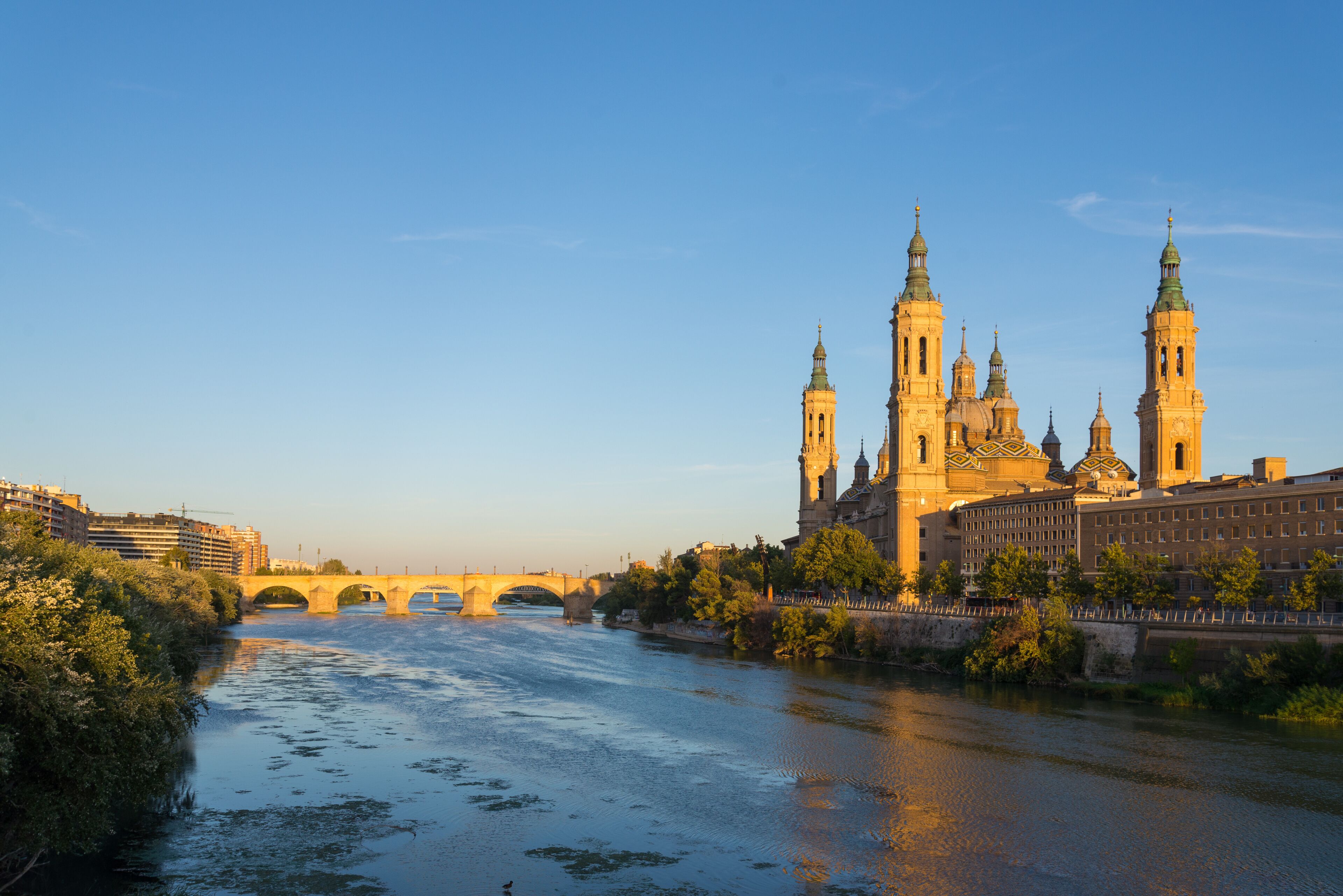 Riverside of Ebro river where Basílica de Nuestra Señora del Pilar, baroque basilica is famous pilgrimage site, is located and Puente de Piedra, stone bridge during sunset time in Zaragoza, Spain.